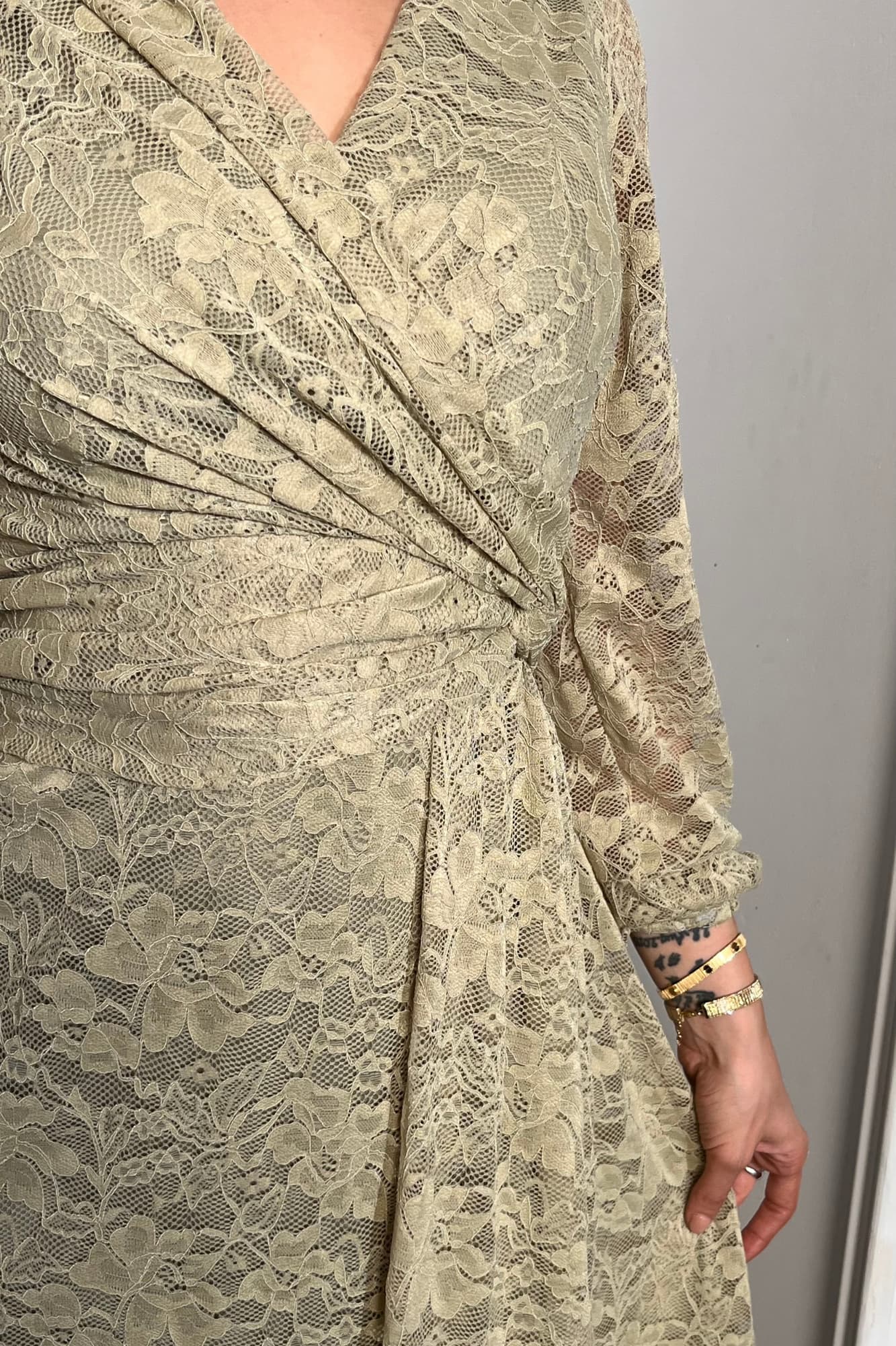 فستان طويل من الدانتيل بلون أخضر فاتح هادئ، يعكس أنوثة راقية ولمسة رومانسية ناعمة يتميّز بقصّة لفّ (Wrap) أنيقة مع عقدة جانبية تبرز الخصر